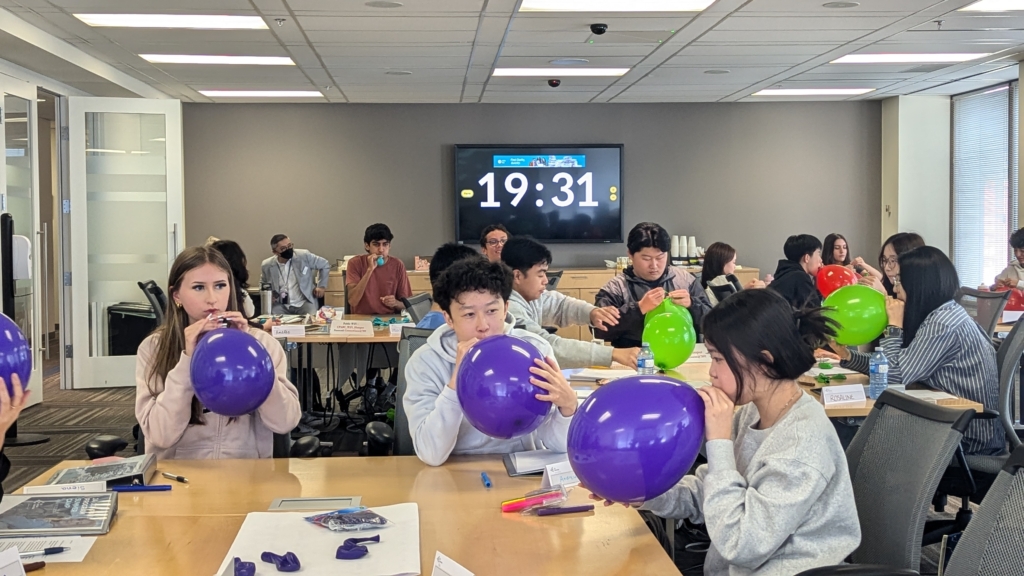 Students participating in a team-building activity at the JA Company Program, inflating colorful balloons while a countdown timer is visible in the background.